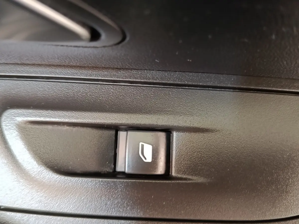 Gros plan sur le bouton de commande de lève-vitre électrique noir dans l'habitacle d'une Peugeot 2008 bleu.