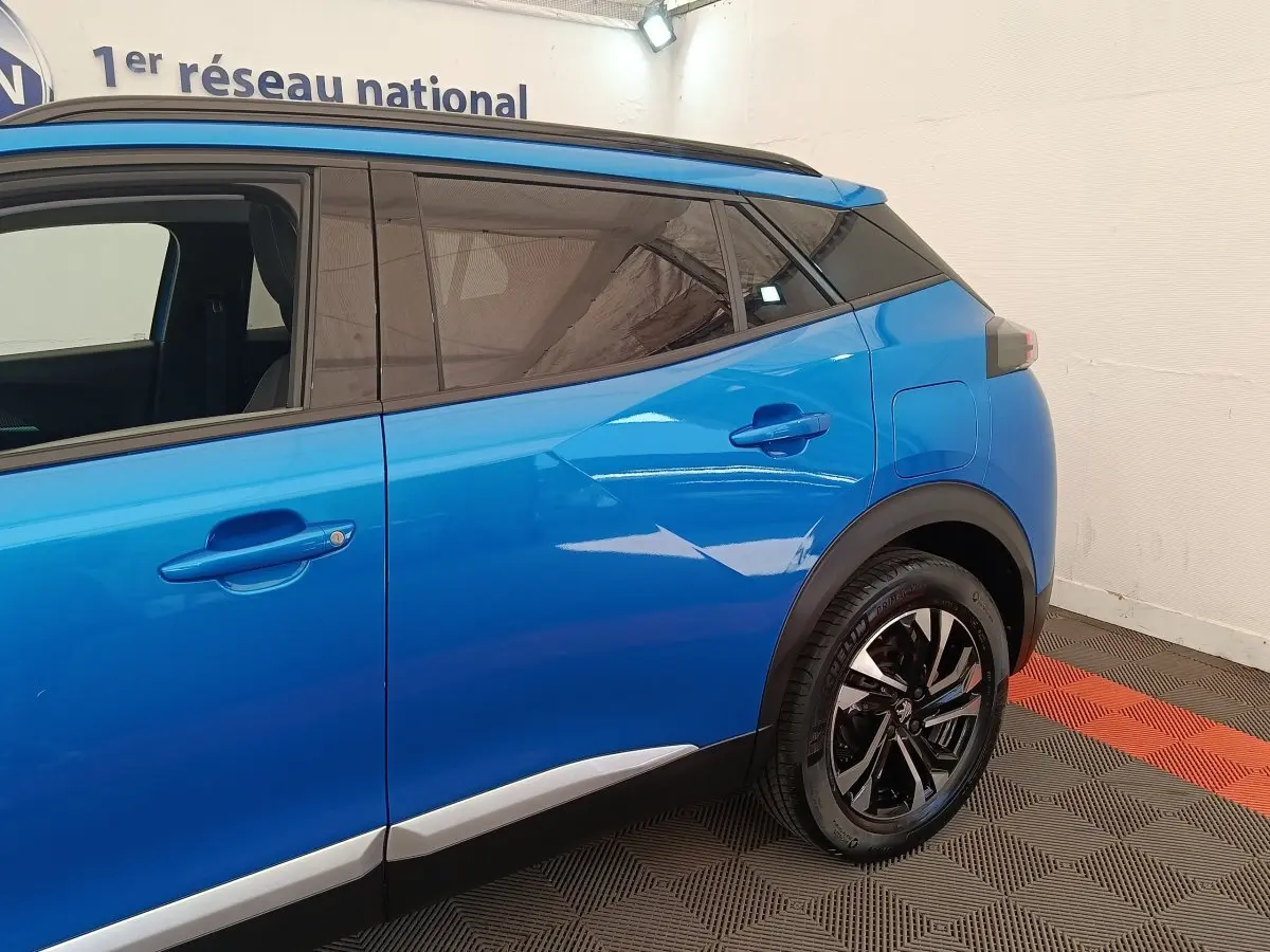 Vue côté droit arrière d’un Peugeot 2008 bleu avec jantes noires et vitres teintées dans un showroom.