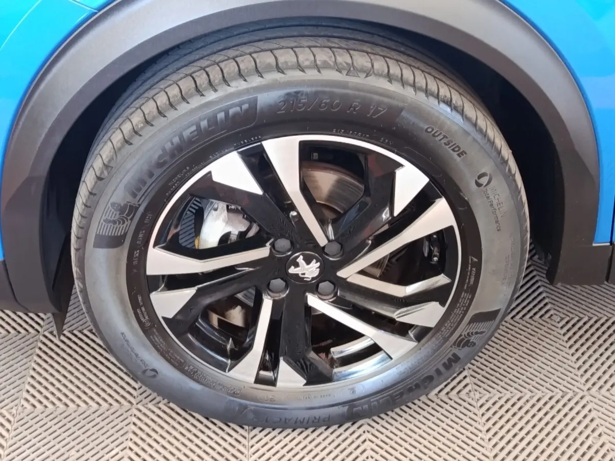 Gros plan sur la roue avant droite d'une Peugeot 2008 bleu, jante alliage noire et argentée avec pneu Michelin.