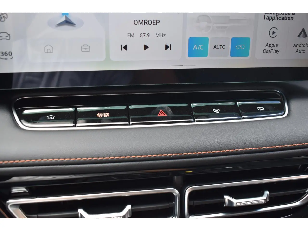 Gros plan sur la console centrale du MG Motor EHS gris 2026, avec boutons de climatisation et finition cuir avec surpiqûres orange.