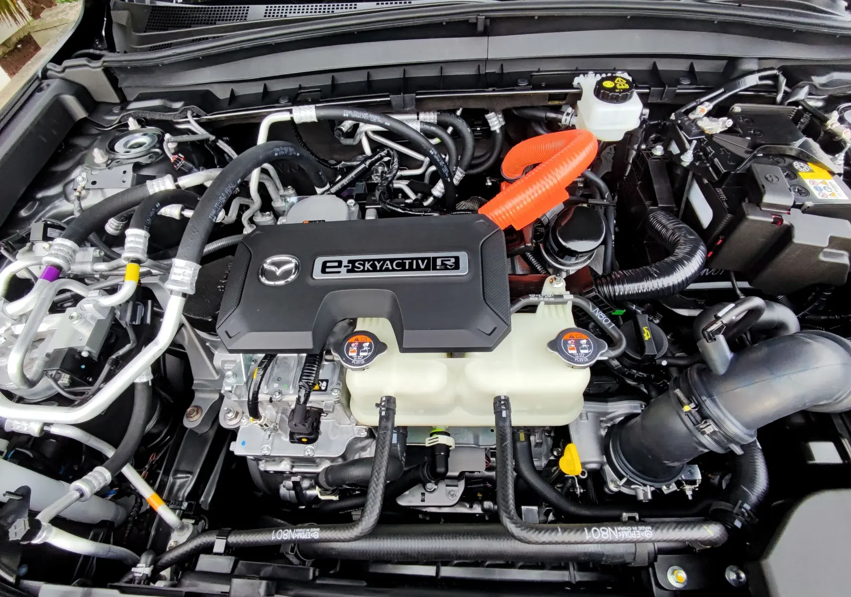 Vue rapprochée du moteur hybride rechargeable e-SKYACTIV du Mazda MX-30 gris foncé 2023, avec câbles orange visibles.