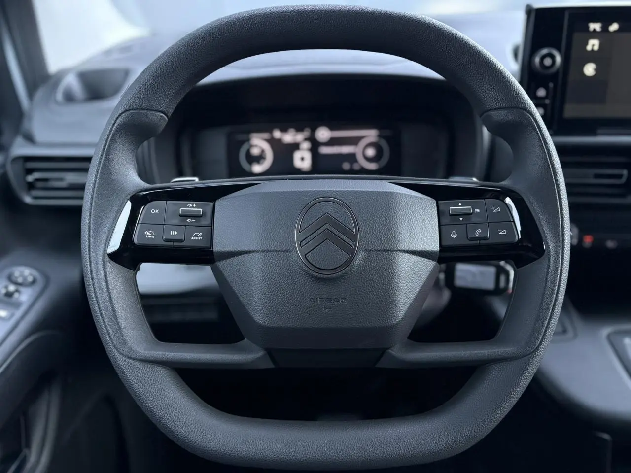 Vue rapprochée du volant multifonctions noir du Citroën Berlingo 2025 avec tableau de bord digital en arrière-plan.