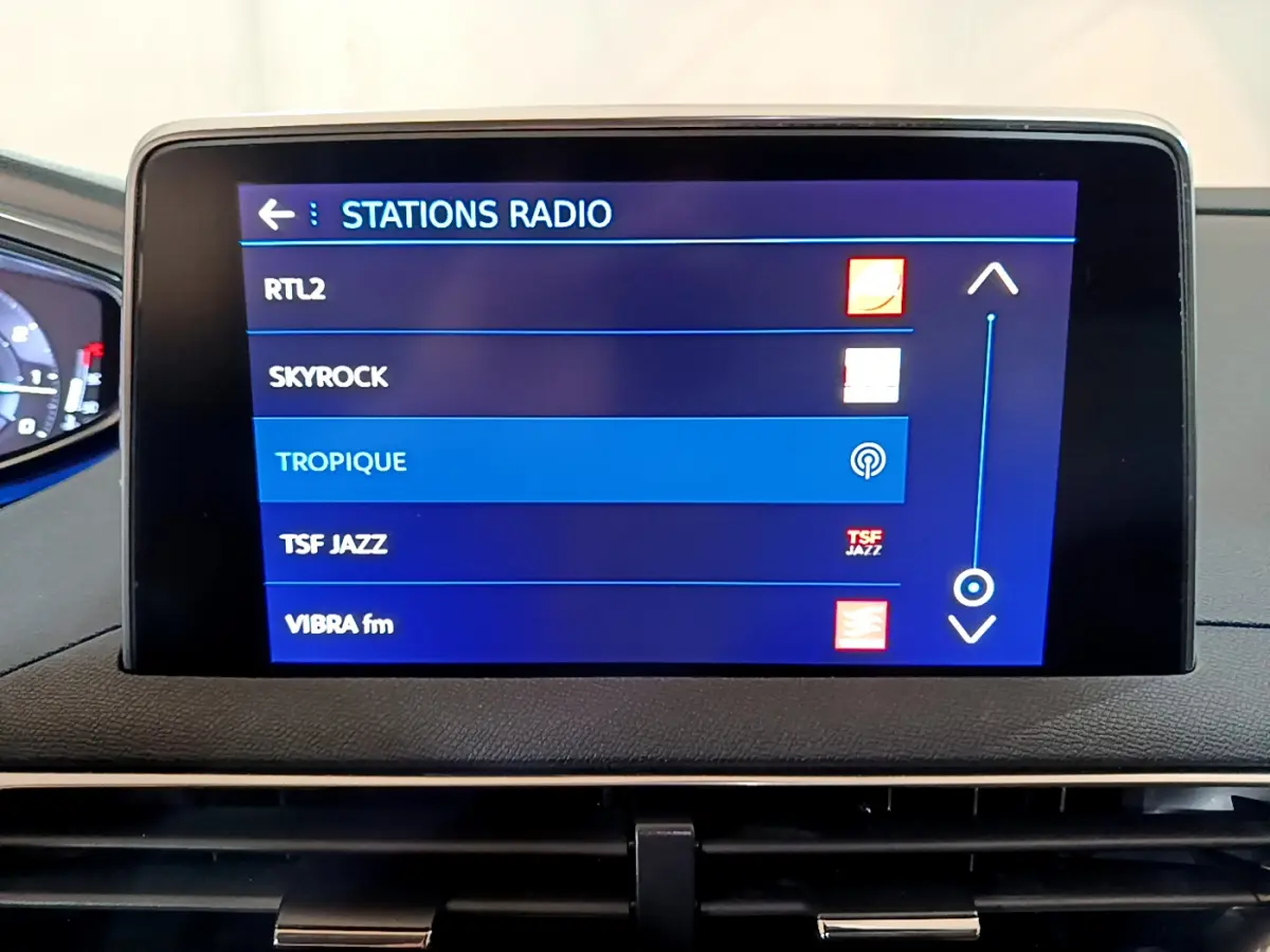 Écran tactile central affichant les stations radio dans l’habitacle d’un Peugeot 5008 gris clair, vue frontale rapprochée.
