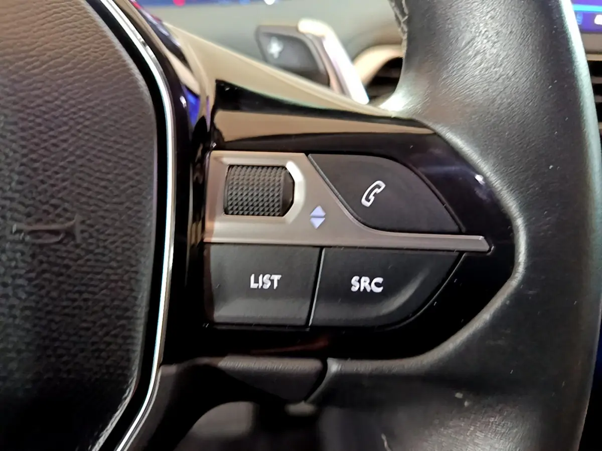 Gros plan sur les commandes gauche du volant cuir noir du Peugeot 5008 gris clair, boutons LIST, SRC et téléphone visible.