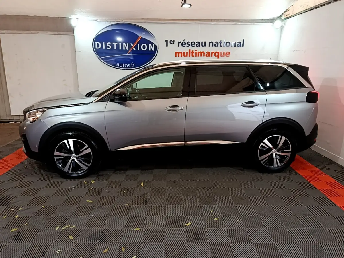 Vue de profil côté gauche d'un Peugeot 5008 gris clair stationné en intérieur avec jantes alliage et vitres teintées.