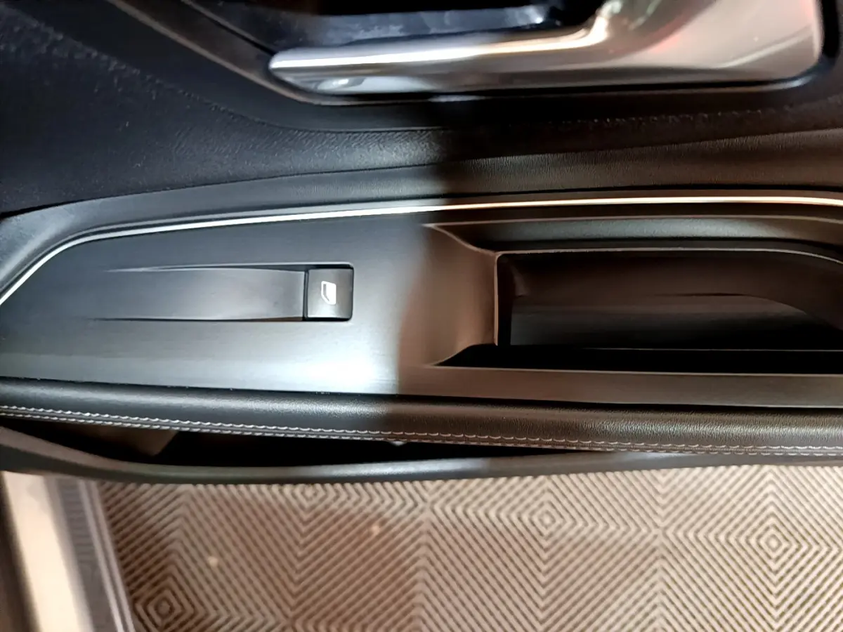 Gros plan sur la poignée intérieure et commande de vitre côté gauche du Peugeot 5008 gris clair, finition Allure.