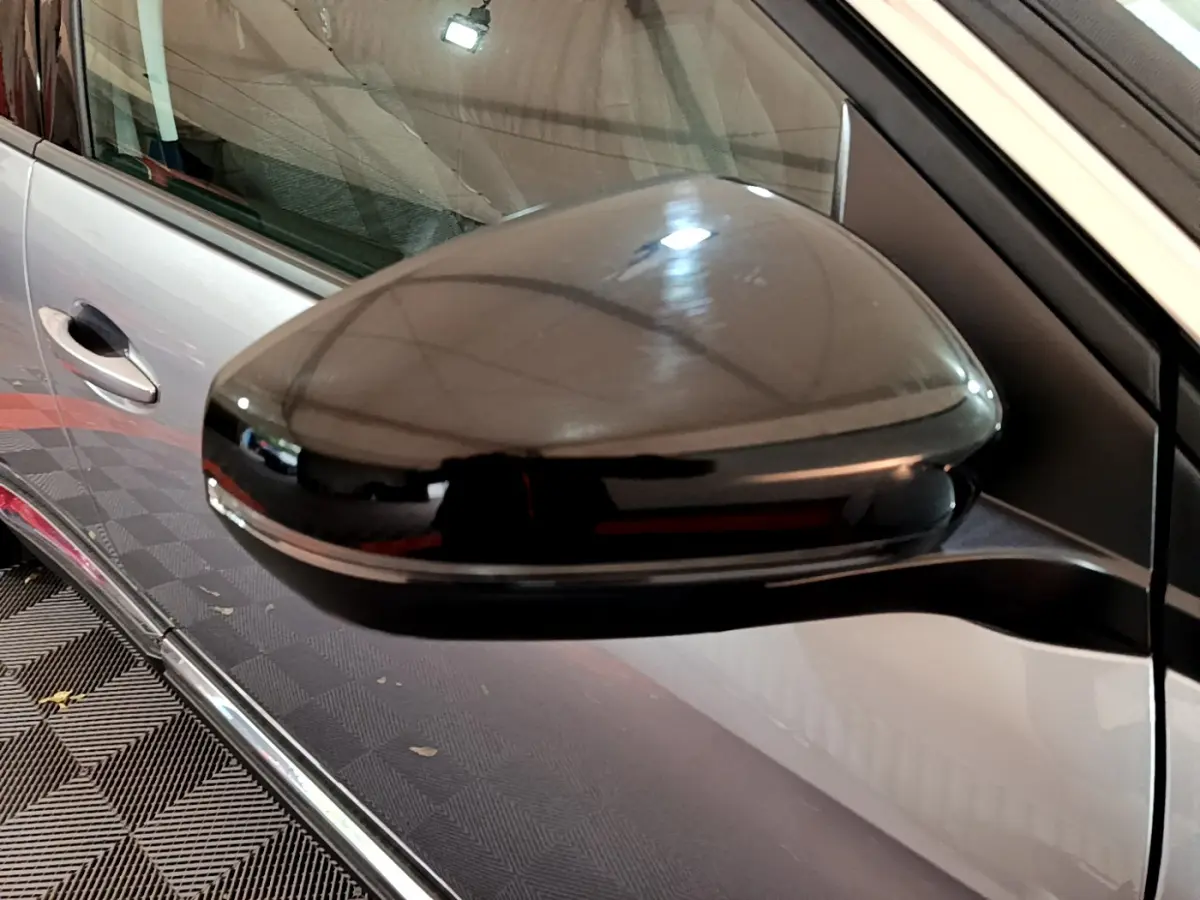 Rétroviseur noir brillant côté gauche d’un Peugeot 5008 gris clair vu de près, avec poignée de porte visible en arrière-plan.