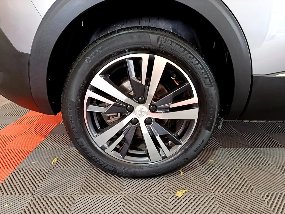Gros plan sur la roue avant droite du Peugeot 5008 gris clair, soulignant la jante alliage bicolore et le pneu Michelin.