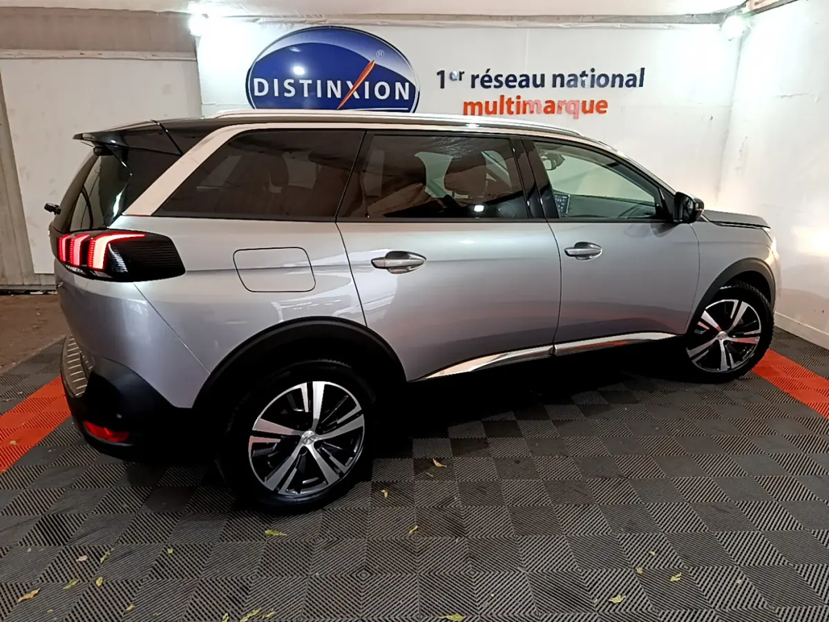 Peugeot 5008 gris clair vue de profil droit en intérieur, avec feux arrière allumés et jantes alliage.