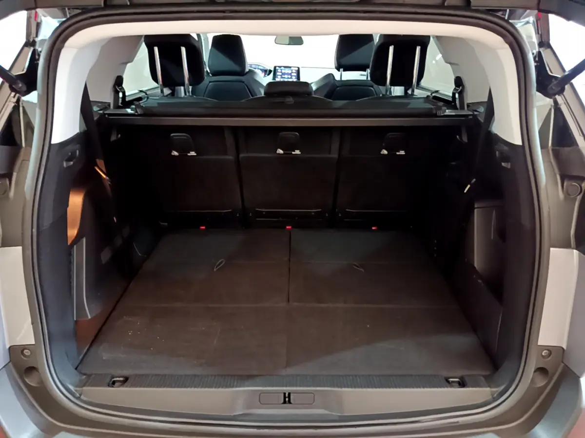 Coffre ouvert vu de l'arrière d'un Peugeot 5008 gris clair, montrant la 3ème rangée de sièges rabattue et plancher plat.