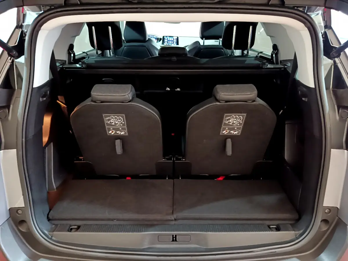 Vue arrière du coffre ouvert d'un Peugeot 5008 gris clair, montrant la 3ème rangée de sièges individuels rabattus.