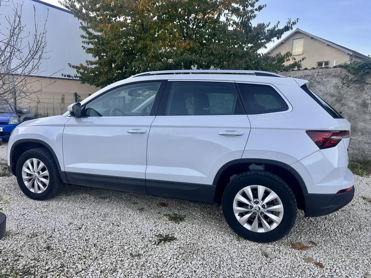 Vue de profil côté gauche d’un Skoda Karoq blanc 2024 garé sur un sol gravillonné avec jantes alliage.