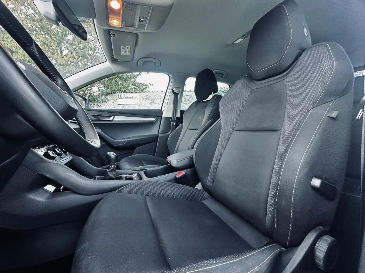 Vue intérieure côté droit du Skoda Karoq 2024, sièges avant noirs avec coutures blanches et levier de vitesse manuel.