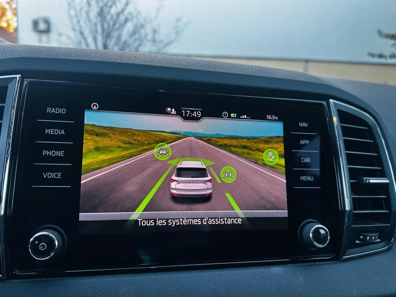 Écran tactile intérieur montrant l'aide au stationnement avec vue arrière virtuelle du Skoda Karoq blanc.