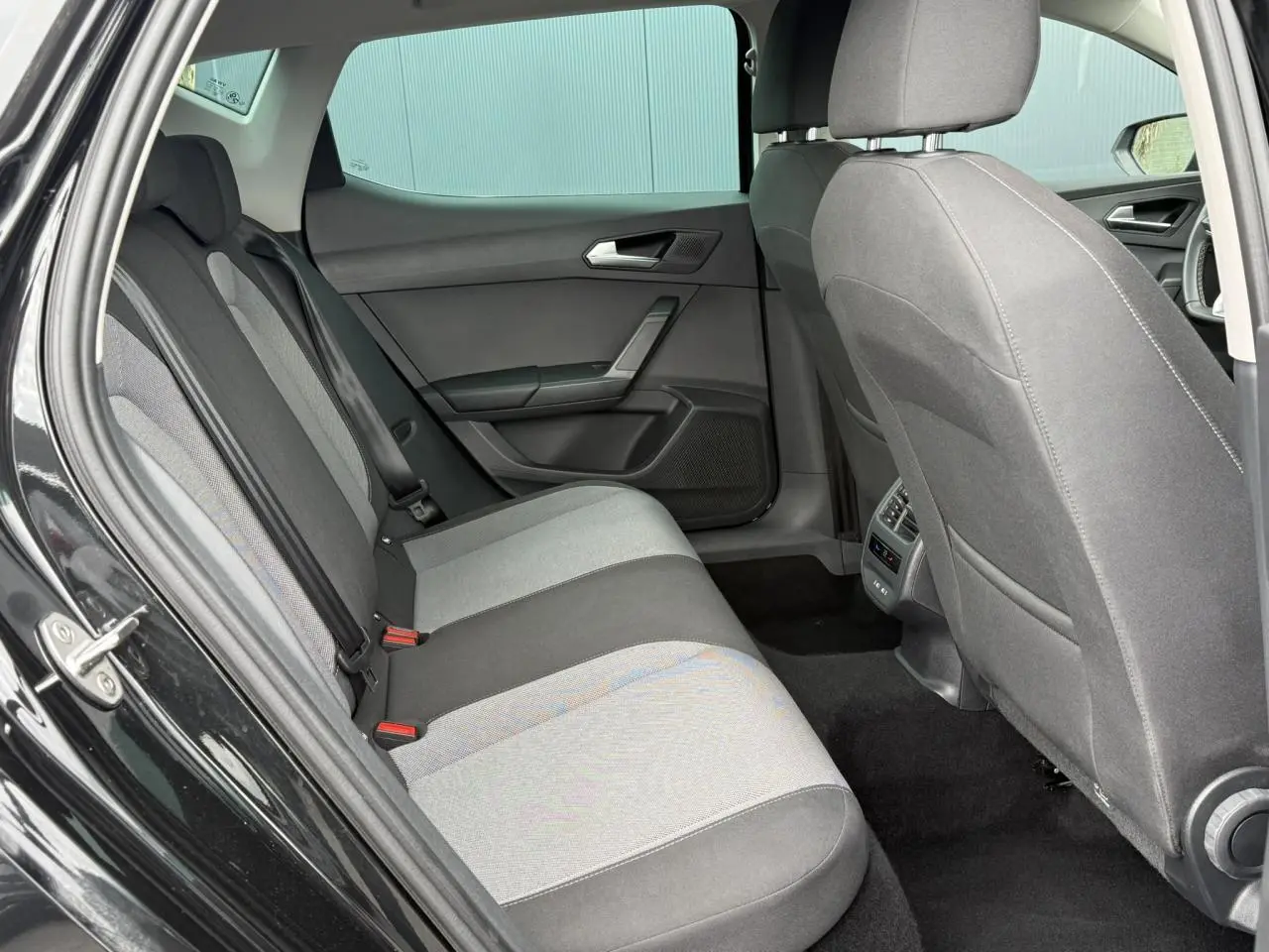 Vue intérieure arrière côté gauche d’une SEAT Leon noir Minuit, montrant les sièges tissu bicolores et les aérateurs arrière.