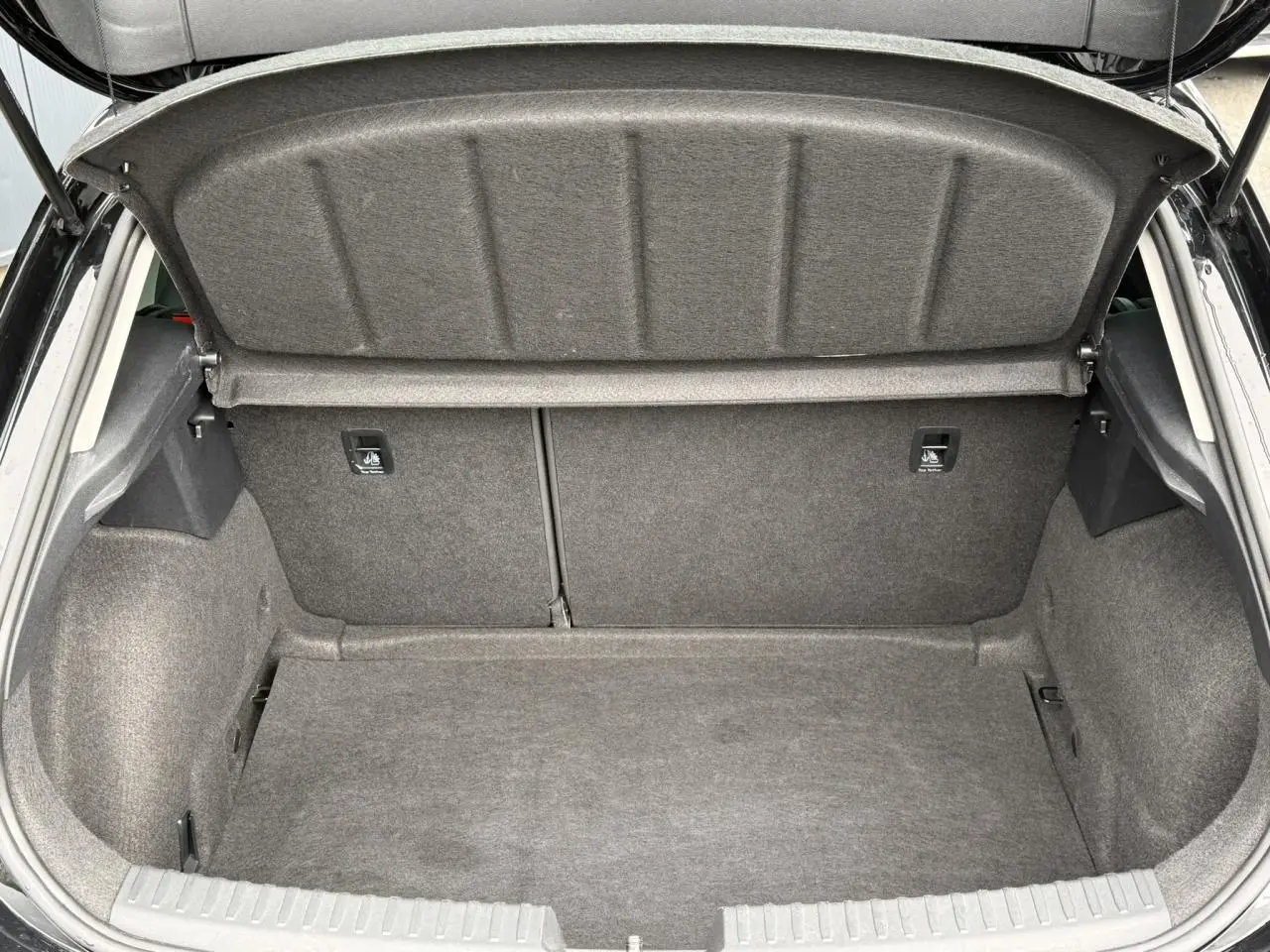 Coffre ouvert vu de l'arrière d'une SEAT LEON noir Minuit, montrant l'espace de chargement vide et la plage arrière relevée.