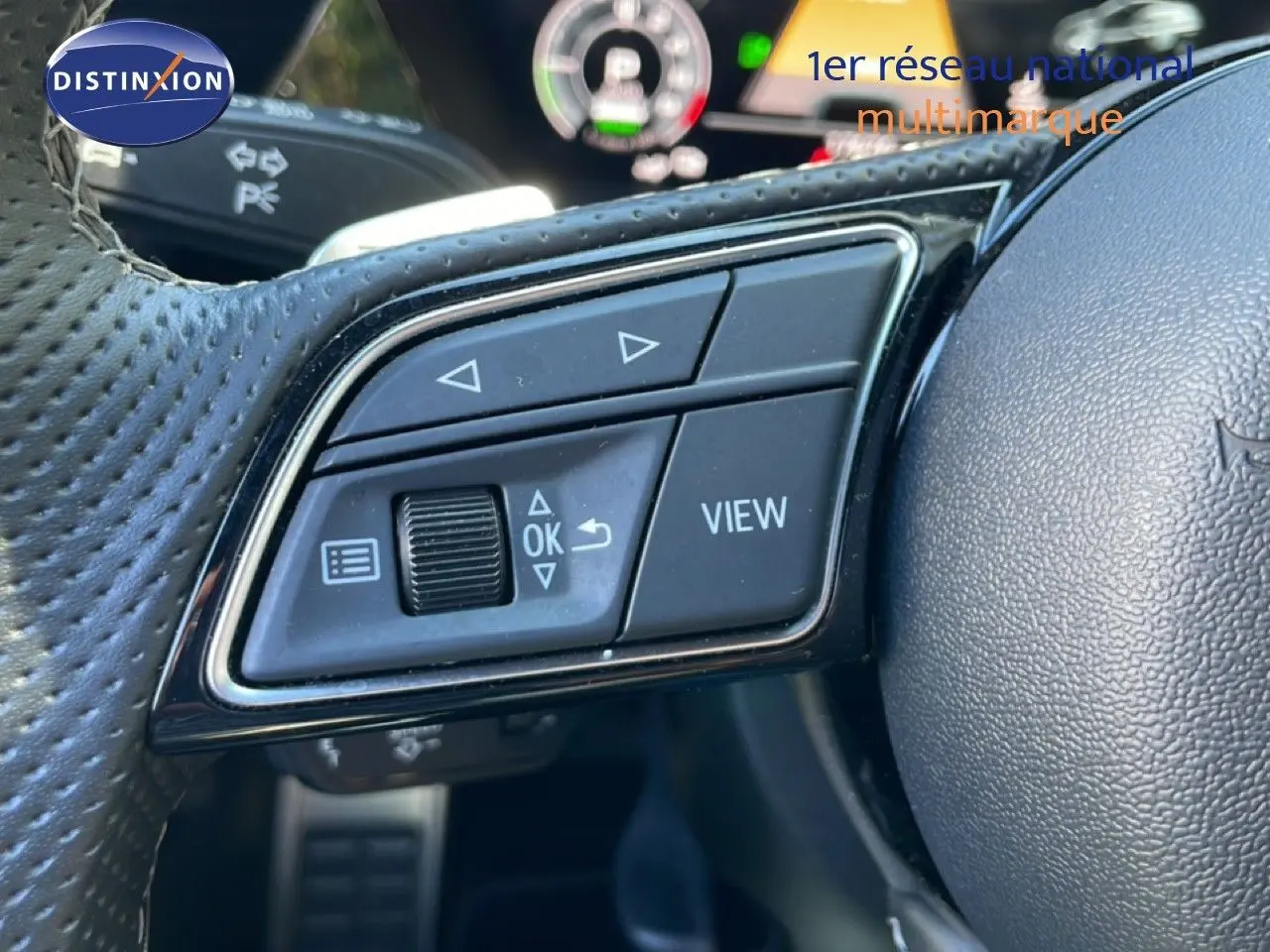 Gros plan sur les commandes gauche du volant en cuir perforé de l'Audi A3 Sportback 2025, avec affichage numérique en arrière-plan.
