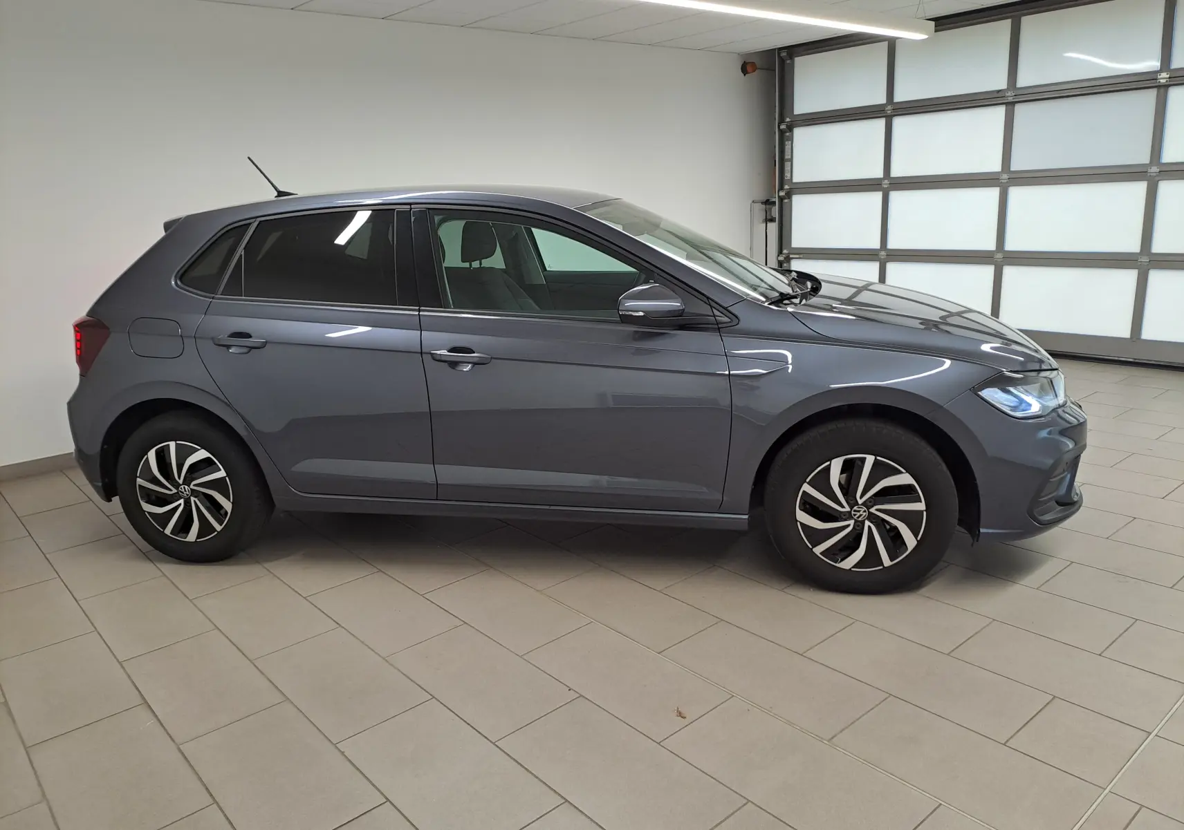 Vue de profil côté gauche d'une Volkswagen Polo gris cendre 2025 avec jantes alliage et vitres teintées en intérieur showroom.