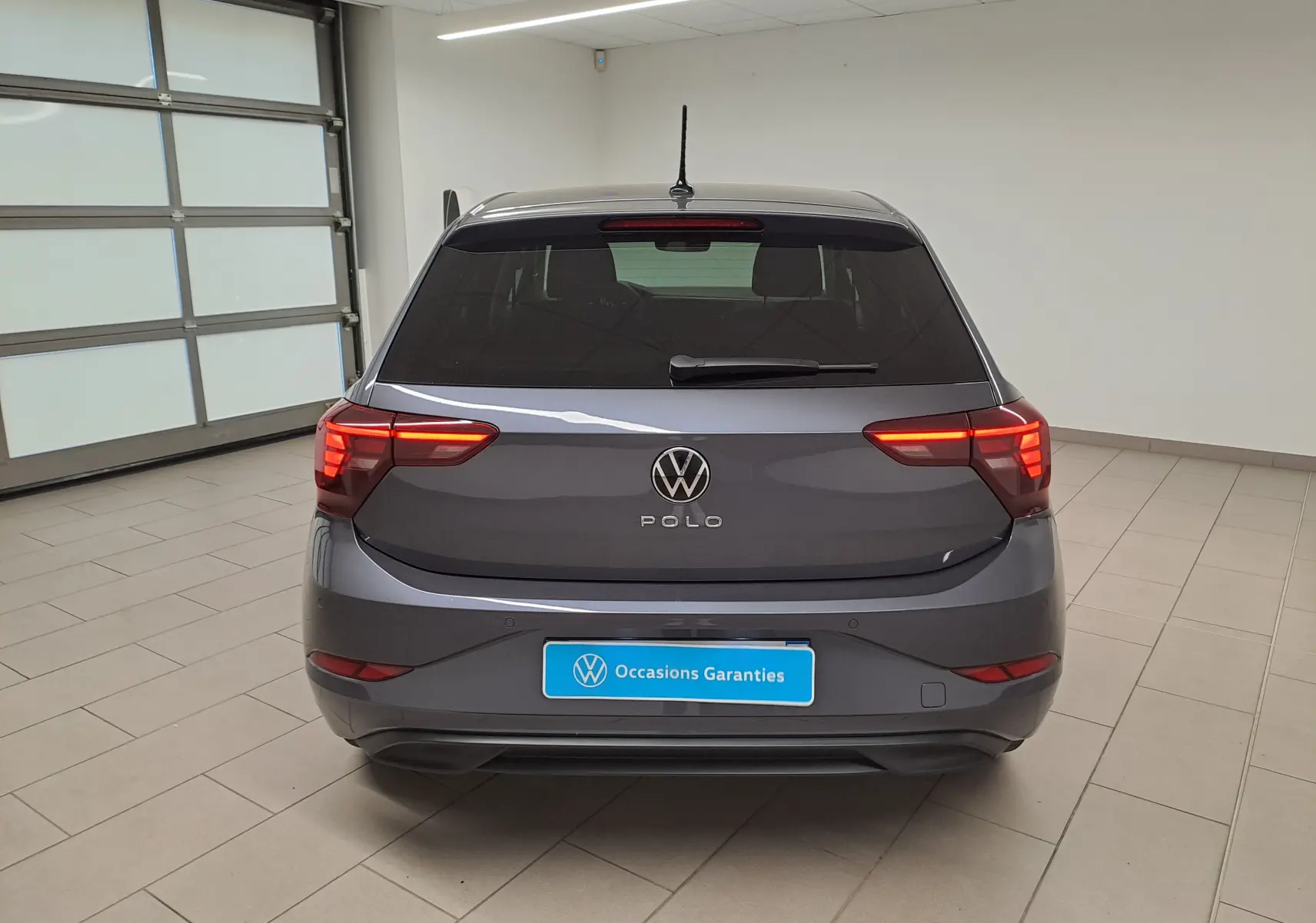 Vue arrière d'une Volkswagen Polo gris cendre 2025 avec feux allumés dans un garage lumineux.