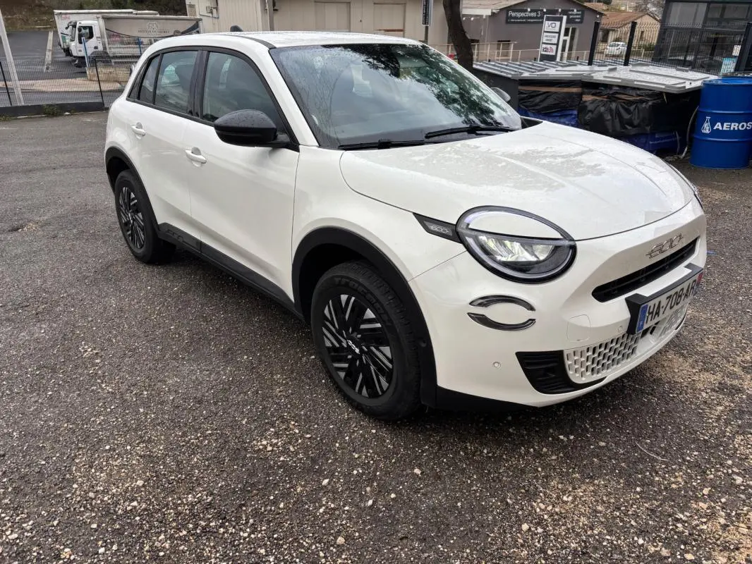 Vue 3/4 avant droit d'une FIAT 600 blanche 2024 avec jantes noires et détails noirs contrastants sur les rétroviseurs et phares.