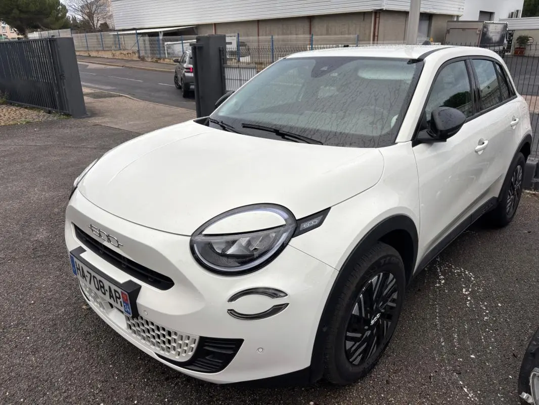 Vue 3/4 avant droite d'une FIAT 600 blanche 2024 avec jantes noires et phares ronds distinctifs.