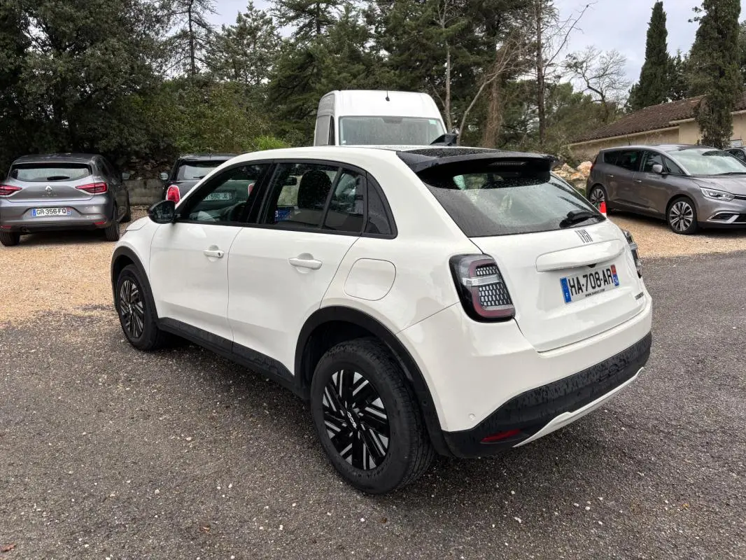 Vue 3/4 arrière droite d'une FIAT 600 blanche 2024 avec toit noir et jantes noires classiques.