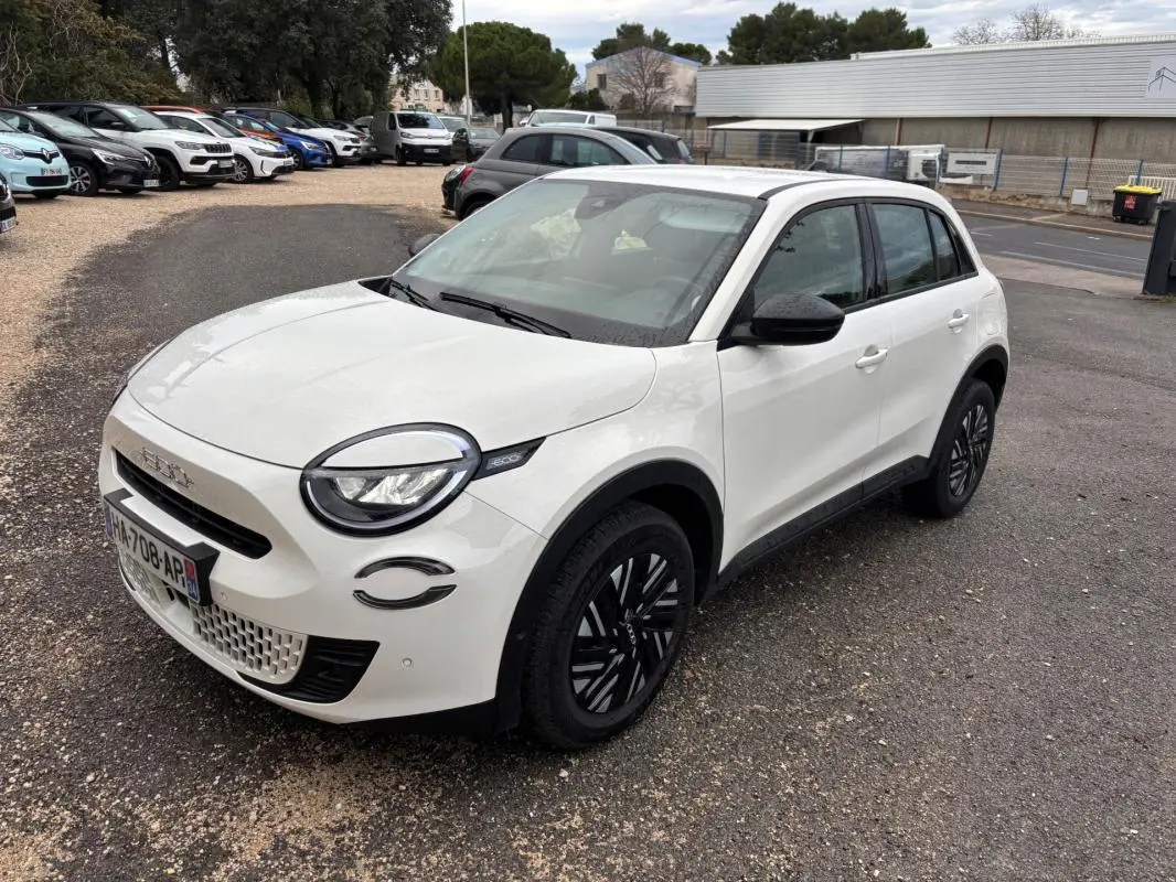Vue 3/4 avant droite d'une FIAT 600 blanche 2024 avec jantes noires et détails noirs autour des phares.