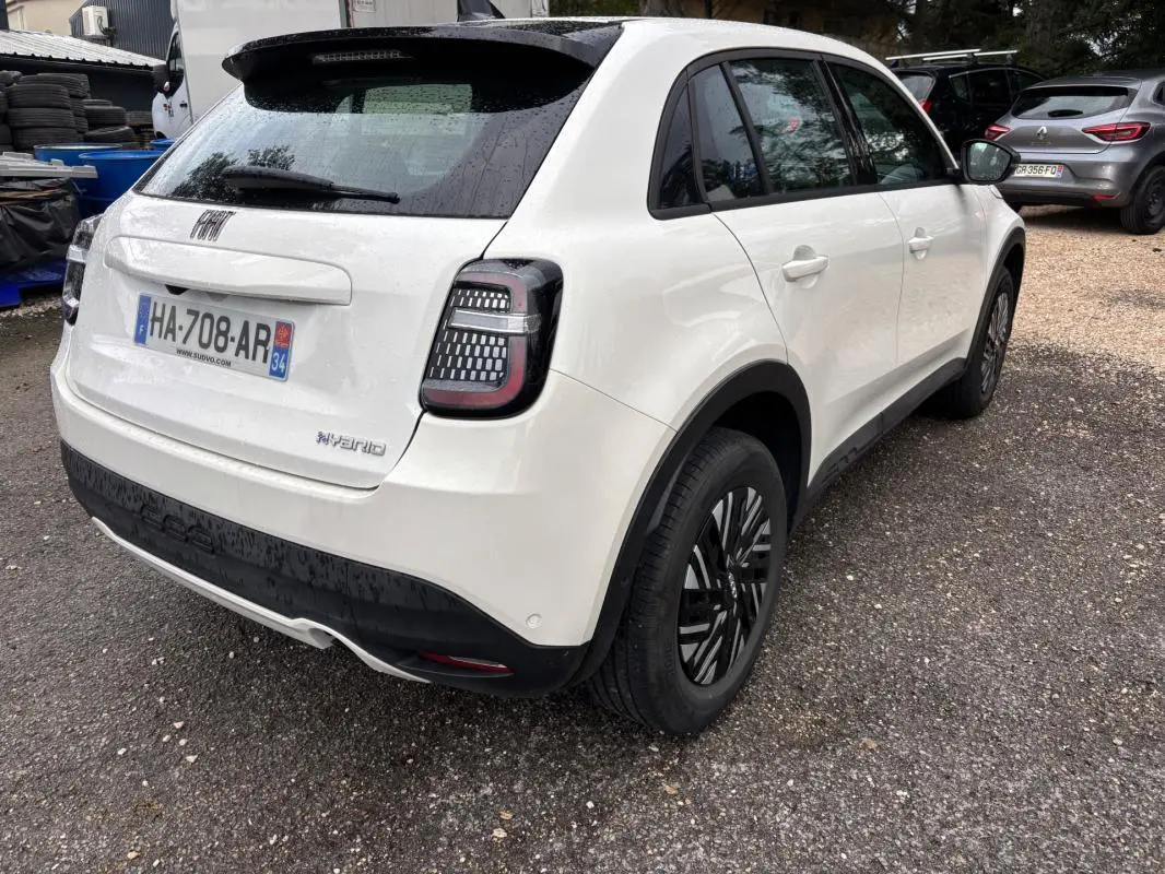 Vue 3/4 arrière droite d'une FIAT 600 blanche 2024 avec feux arrière LED et jantes noires classiques.