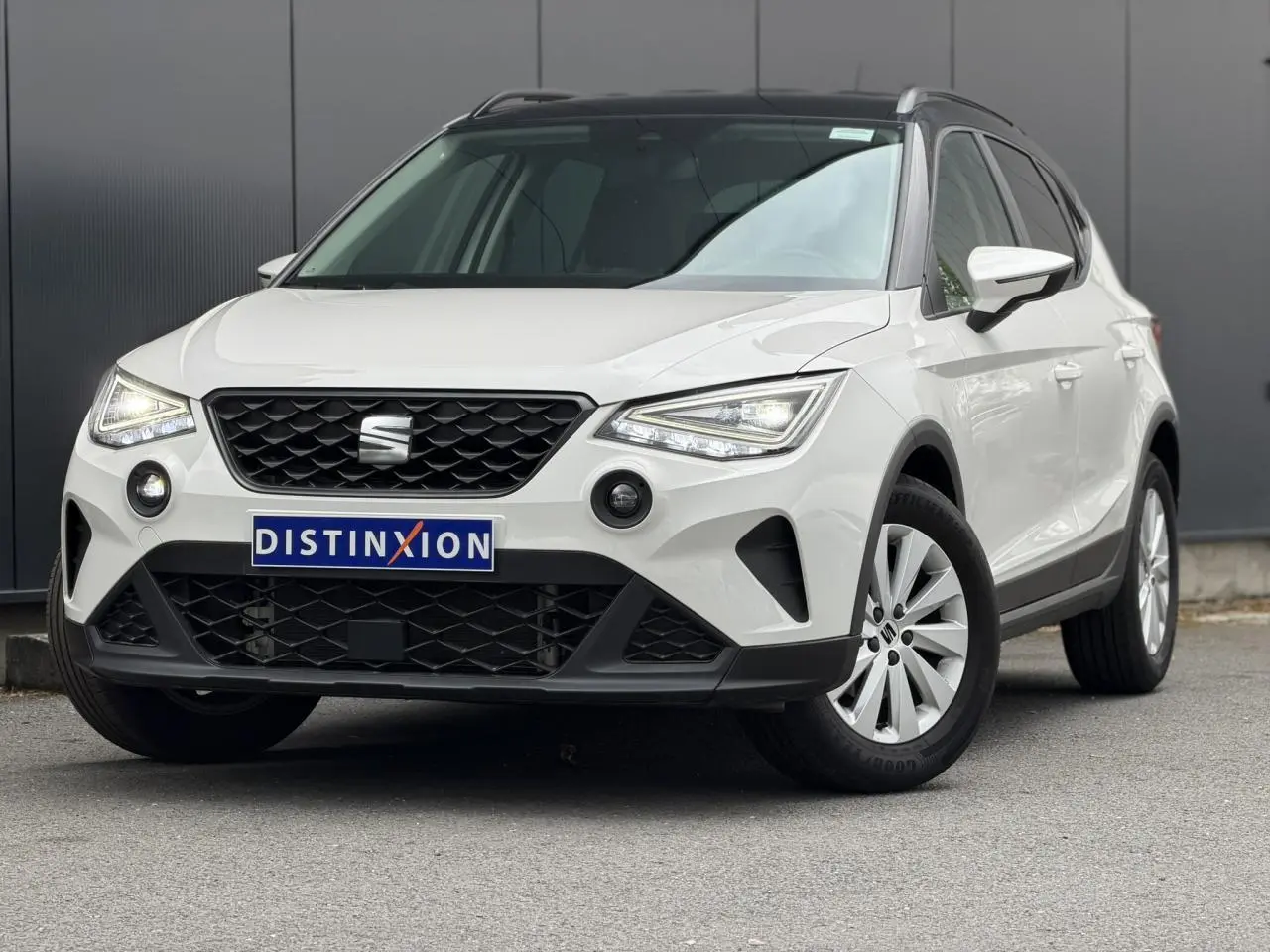 Vue 3/4 avant d’un SEAT Arona blanc avec toit noir, calandre noire et jantes alliage 16 pouces, sur fond urbain.