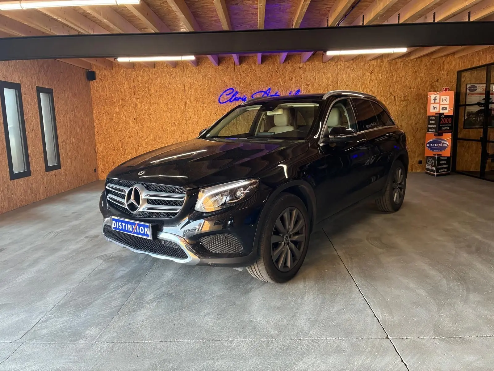 Mercedes GLC 220D Fascination noir en 3/4 avant droit, intérieur cuir beige visible, dans un garage avec murs en bois.