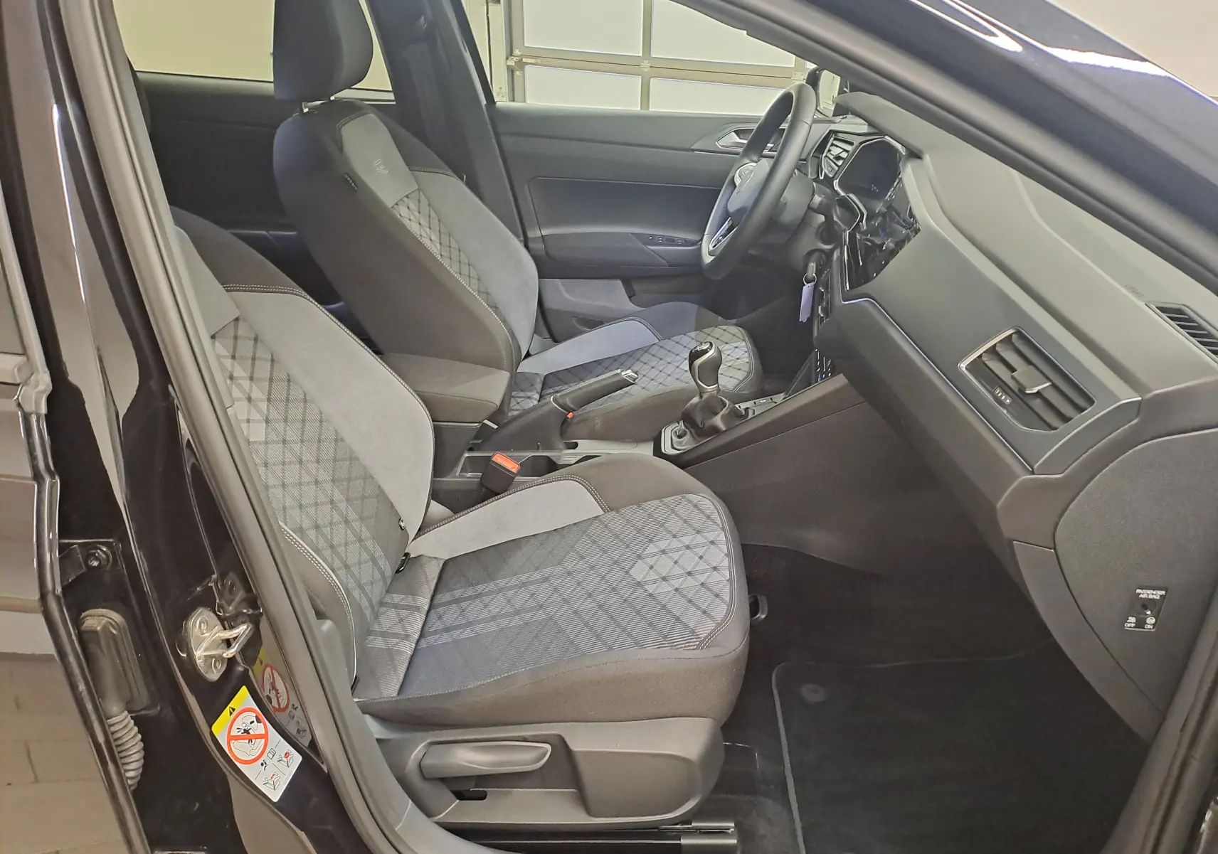Vue intérieure côté conducteur de la Volkswagen Polo 2025 noir intense, sièges tissu à motifs et tableau de bord moderne.