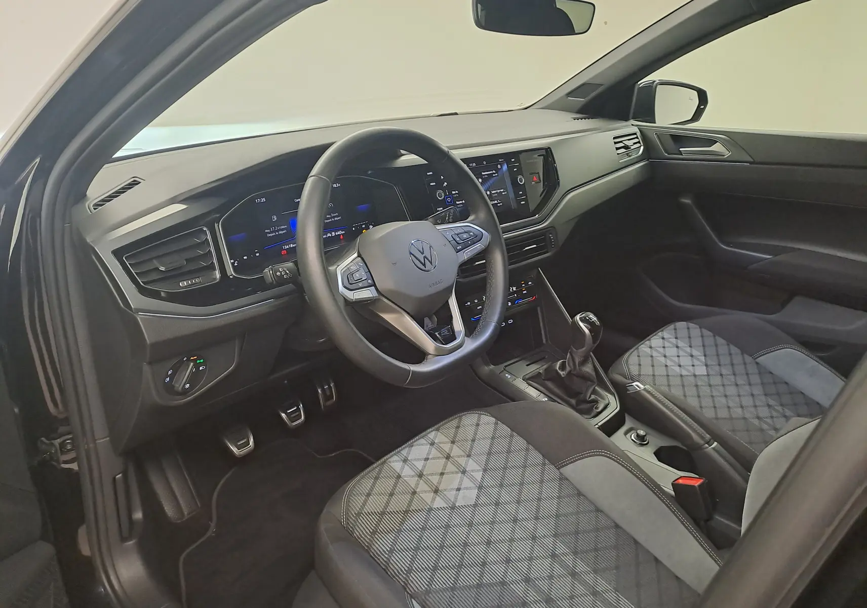 Vue intérieure côté conducteur de la Volkswagen Polo 1.0 TSI R-Line 2025 avec sellerie à motif écossais et boîte manuelle.