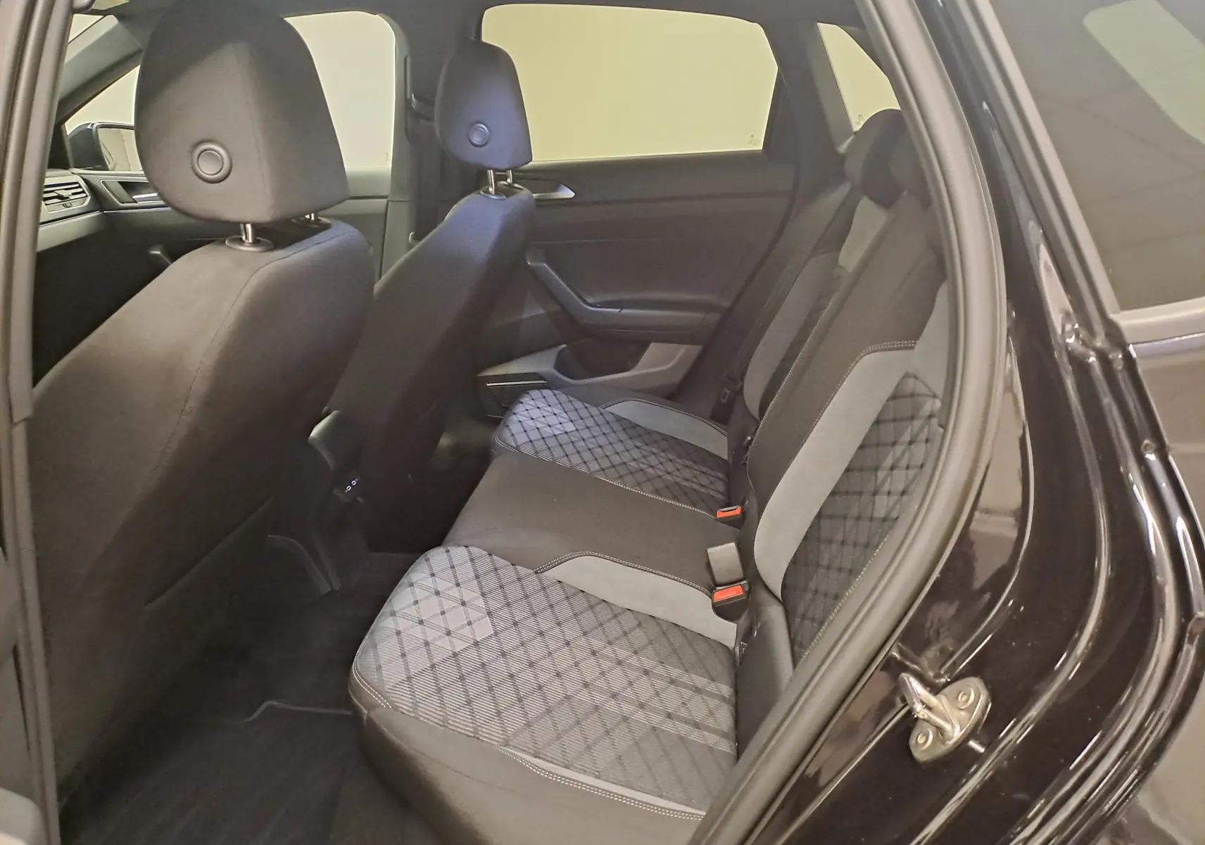 Vue intérieure côté arrière droit de la Volkswagen Polo 2025 noir intense, sièges tissu à motif losange et surpiqûres claires.