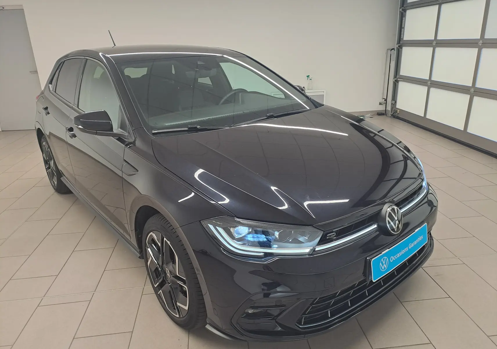 Volkswagen Polo 1.0 TSI R-Line noir intense vue 3/4 avant en intérieur avec jantes spécifiques et phares LED.