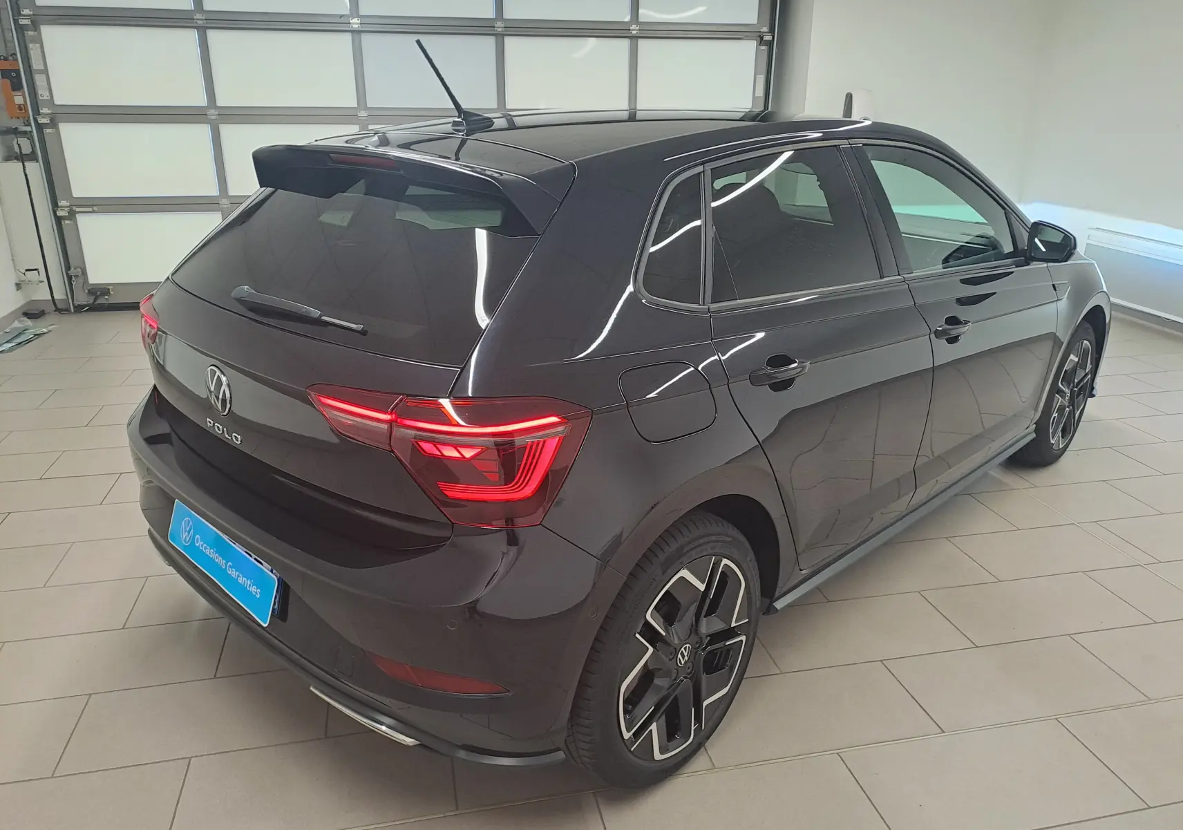 Vue 3/4 arrière droite d'une Volkswagen Polo 2025 noir intense métallisé avec jantes R-Line et feux LED allumés.