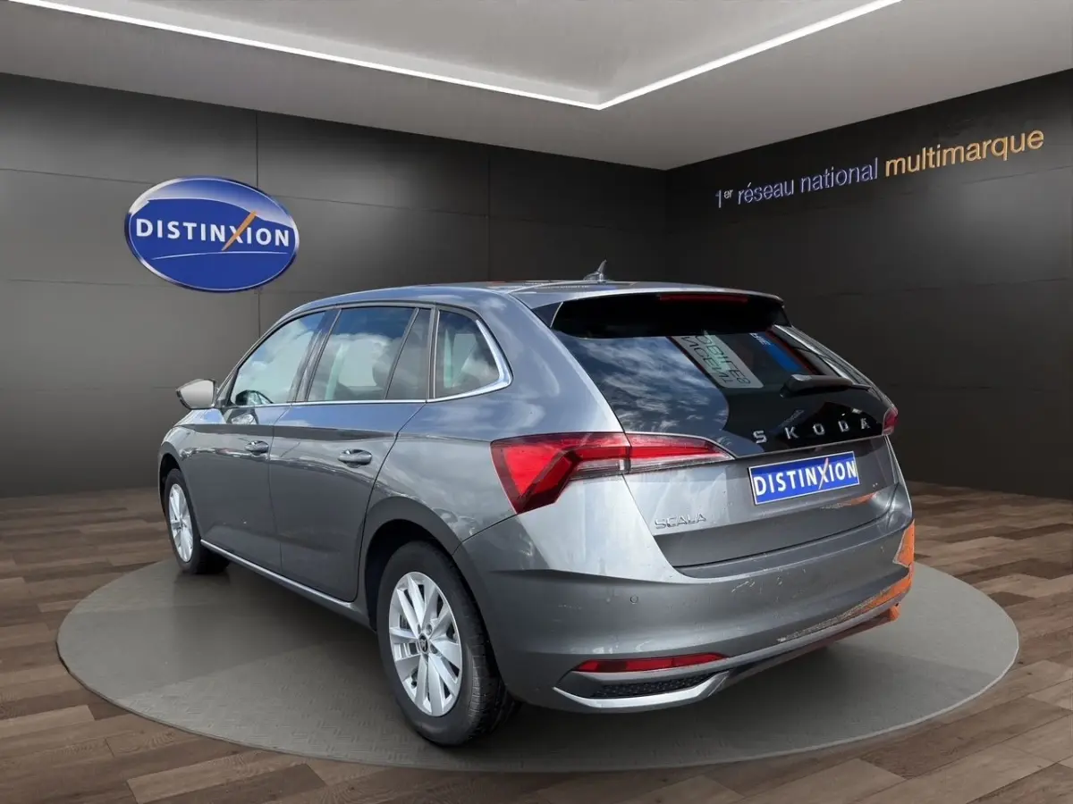 Vue 3/4 arrière gauche d'une Skoda Scala gris foncé avec feux arrière LED et logo distinctif sur fond showroom.