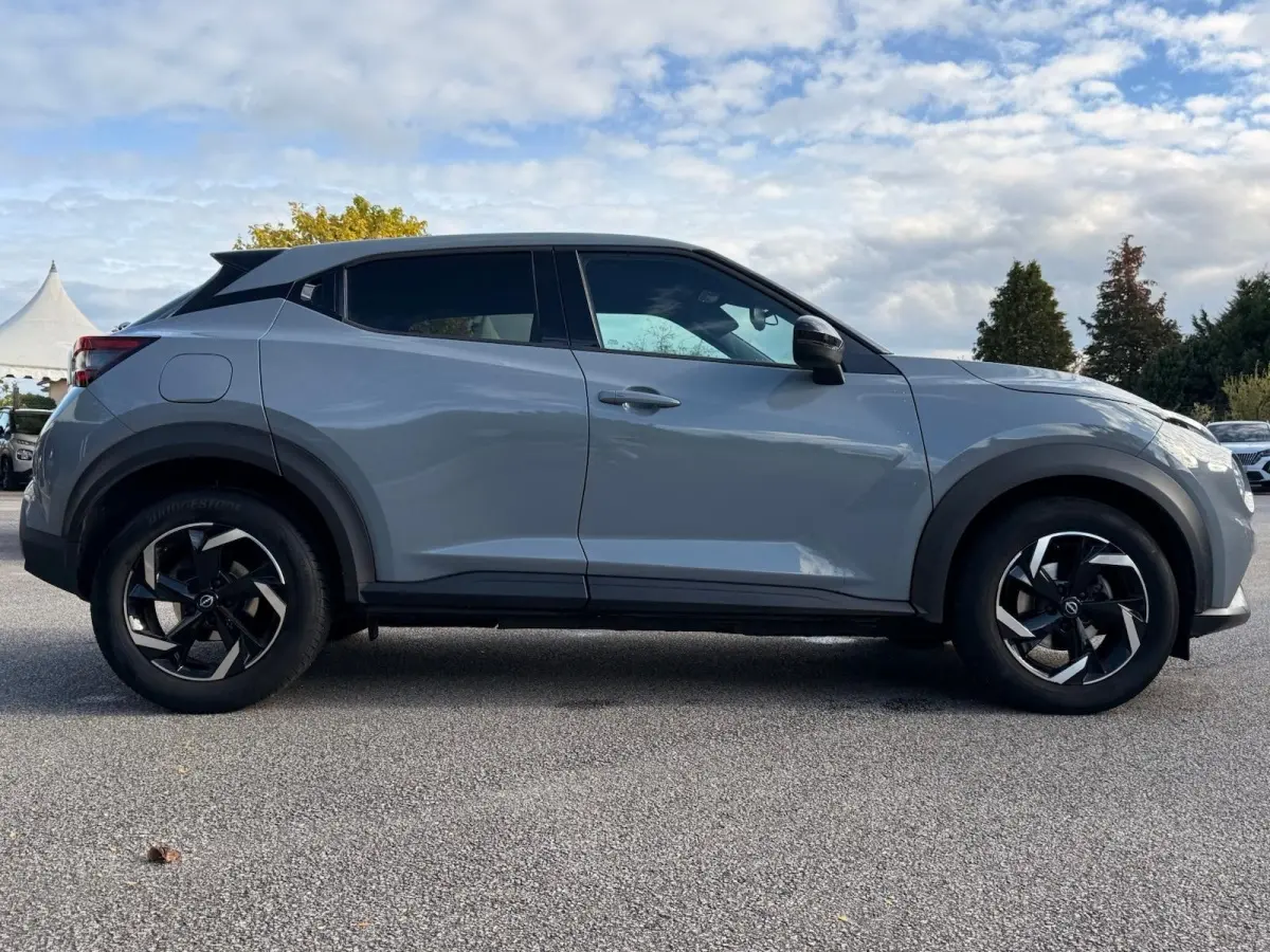 Nissan Juke gris clair vue de profil côté gauche, avec jantes noires et vitres teintées.