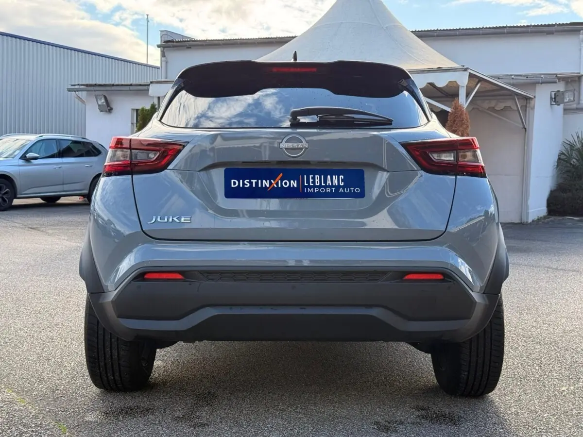 Vue arrière d'un Nissan Juke gris clair 2023 avec feux LED et spoiler de toit visible en extérieur.