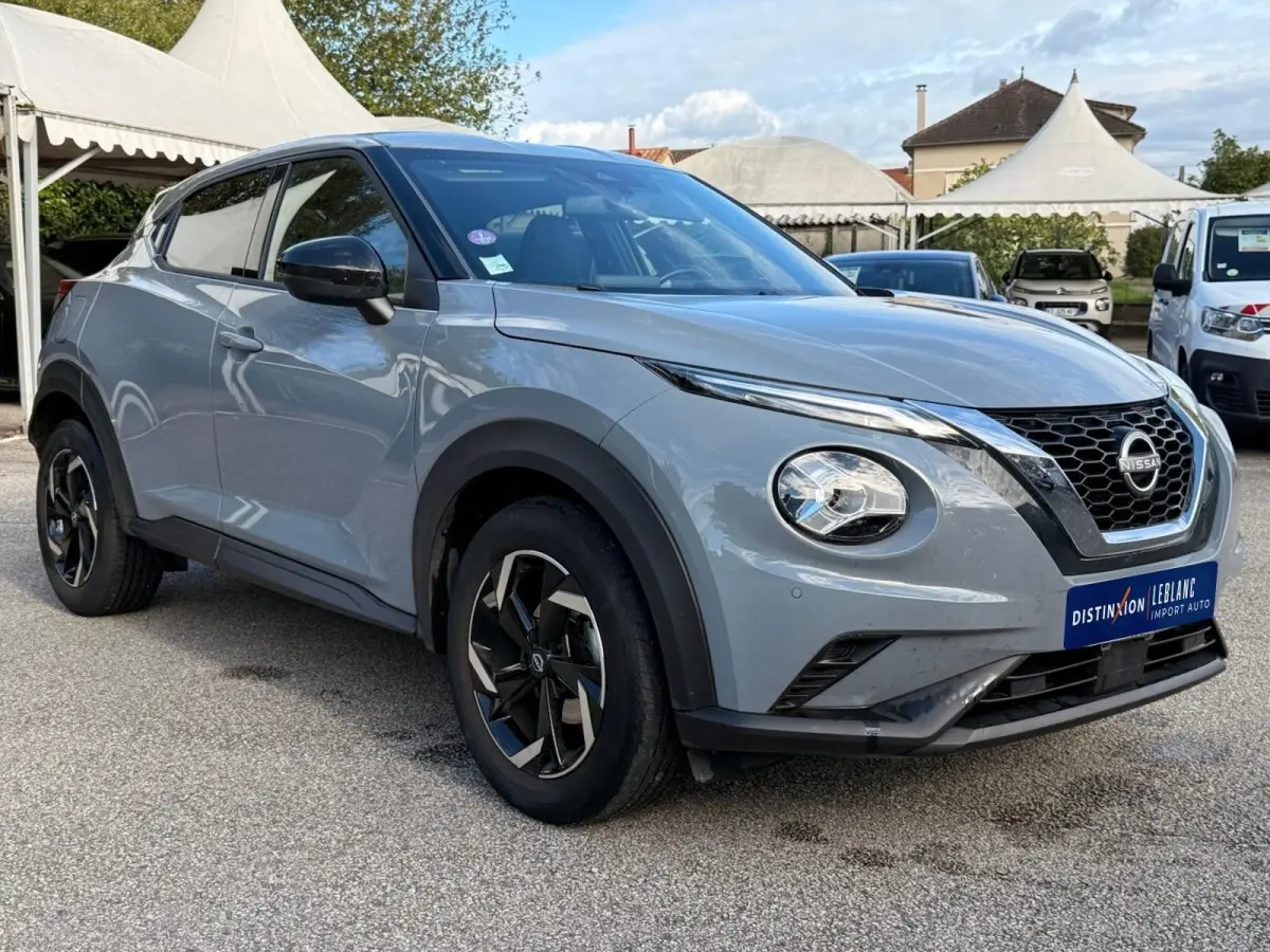Nissan Juke gris clair vue 3/4 avant droit, avec calandre noire en V et jantes noires à motifs argentés.