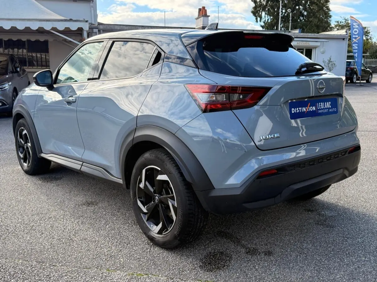 Vue 3/4 arrière droite d'un Nissan Juke gris clair 2023 avec jantes noires et toit noir brillant.