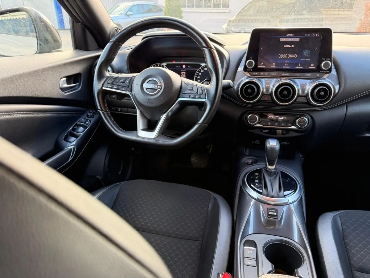 Vue intérieure avant du Nissan Juke gris clair 2023, volant cuir multifonctions et écran tactile central visible.