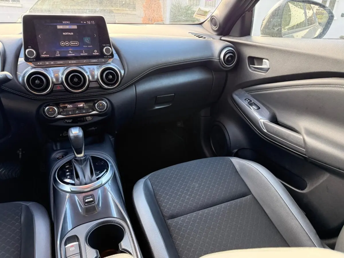 Vue intérieure côté passager du tableau de bord et console centrale du Nissan Juke gris clair avec écran tactile et levier de boîte auto.