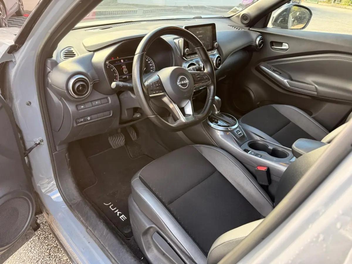 Intérieur côté conducteur du Nissan Juke gris clair 2023, volant cuir multifonctions et écran tactile central visible.