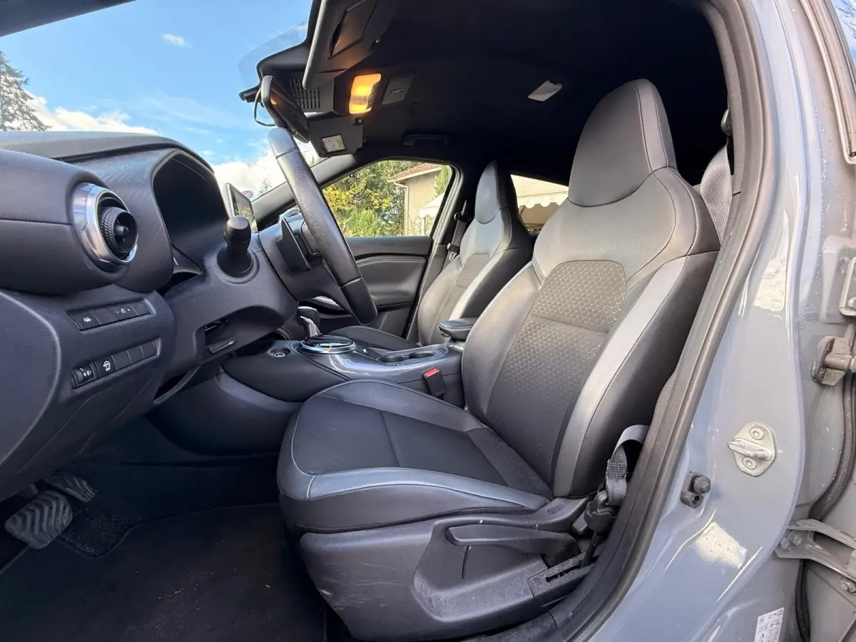 Vue intérieure côté conducteur du Nissan Juke gris clair 2023, mettant en valeur les sièges avant et le tableau de bord.