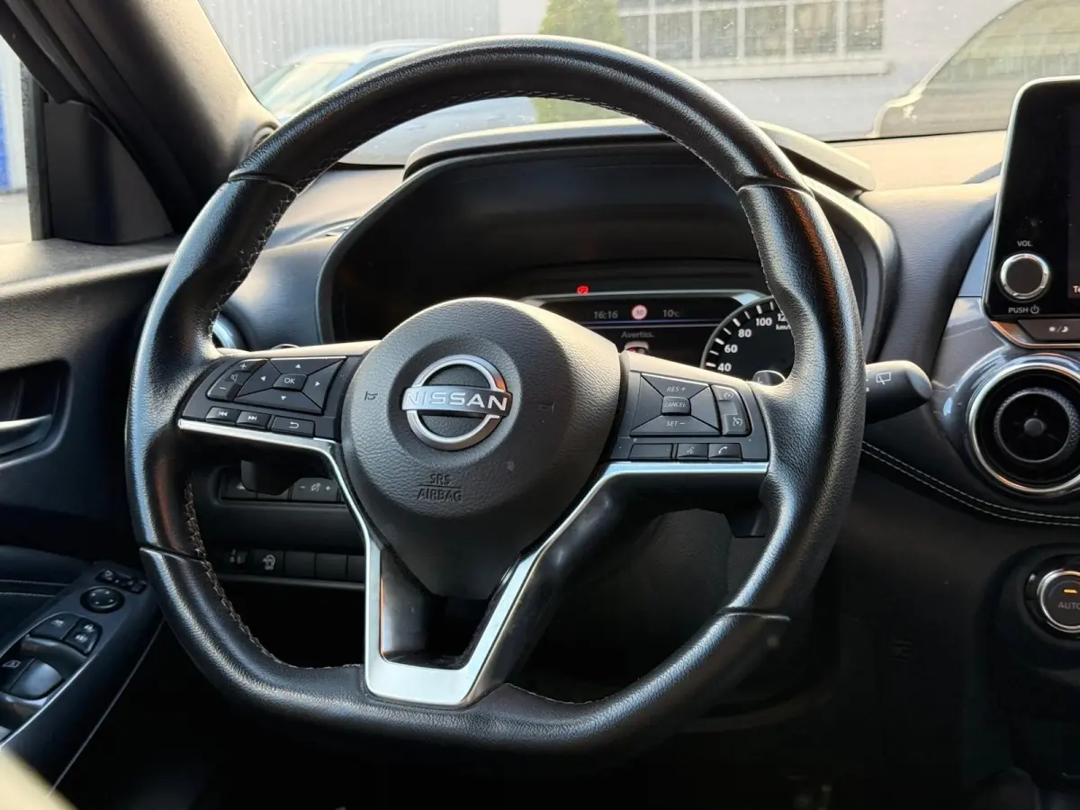 Vue rapprochée du volant cuir noir du Nissan Juke 2023 avec commandes multifonctions et tableau de bord digital.