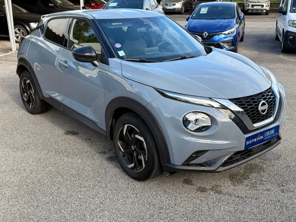 Nissan Juke gris clair vu en 3/4 avant droit, avec calandre noire et jantes alliage noires distinctives.
