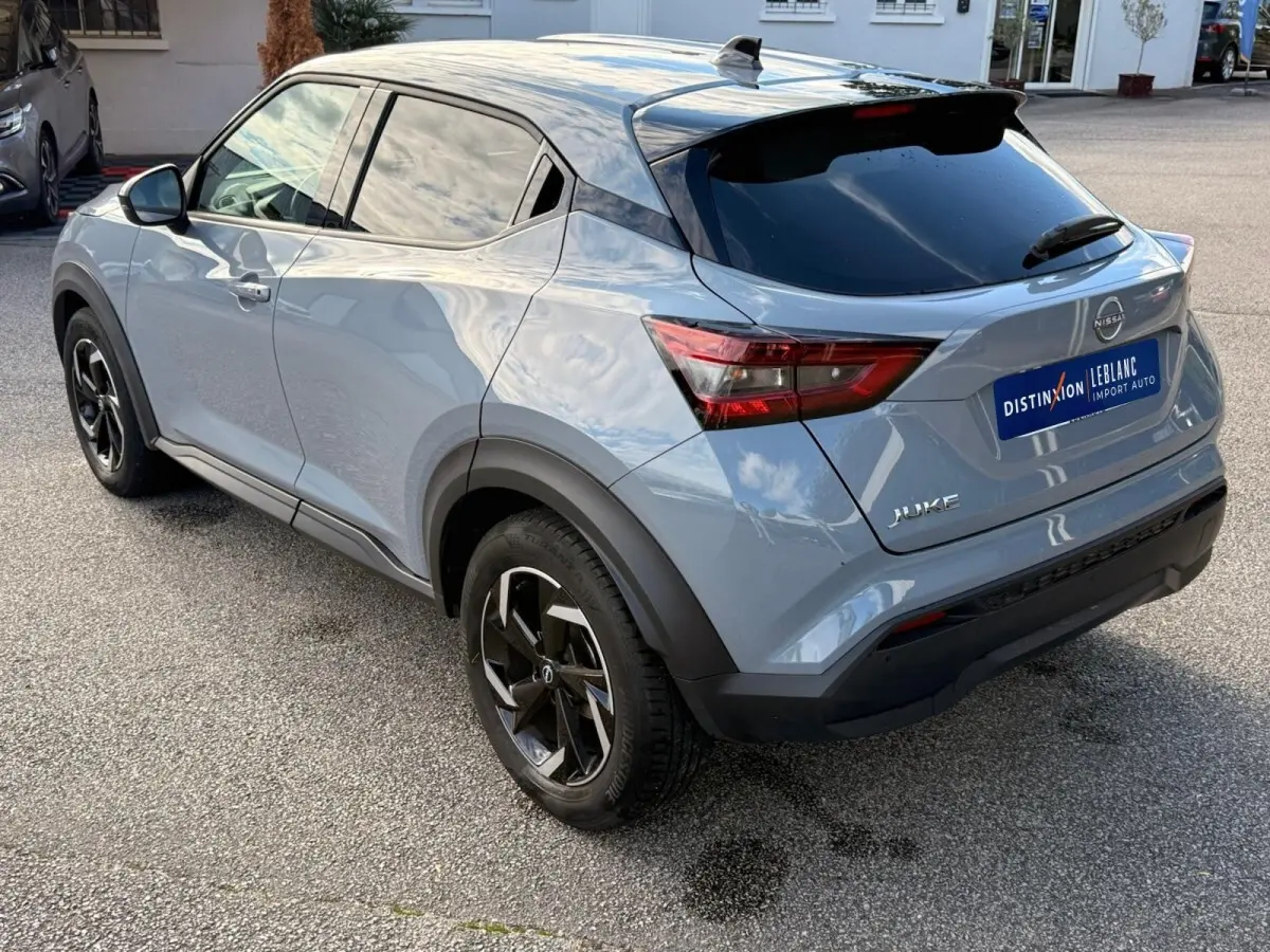 Vue 3/4 arrière droite d'un Nissan Juke gris clair 2023 avec vitres teintées et jantes noires distinctives.