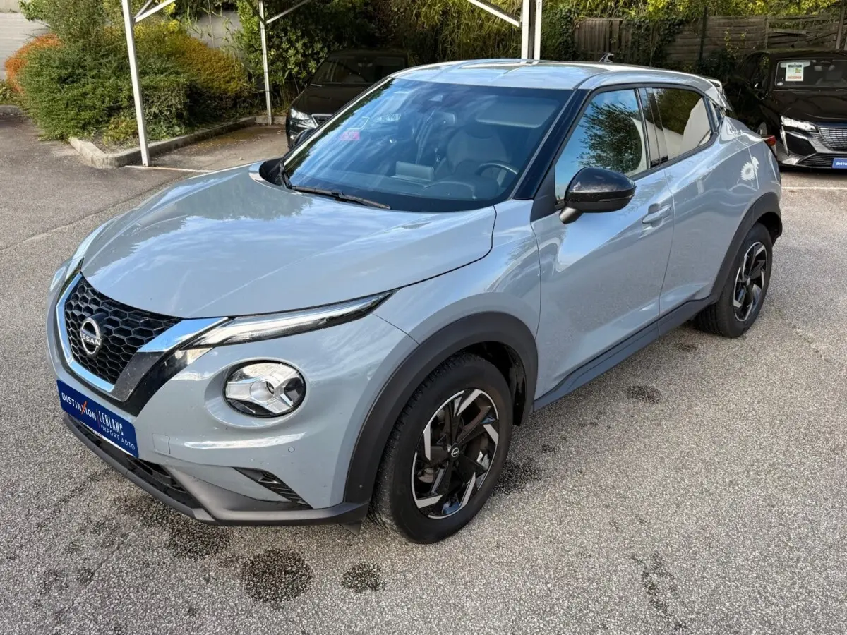 Nissan Juke gris clair en vue 3/4 avant droit, avec calandre noire et jantes alliage bicolores distinctives.