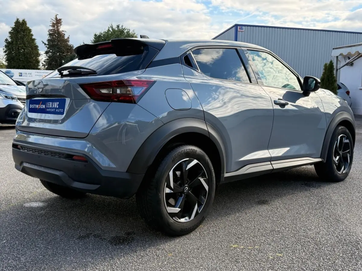 Vue 3/4 arrière droite du Nissan Juke gris clair 2023 avec jantes noires et vitres teintées.