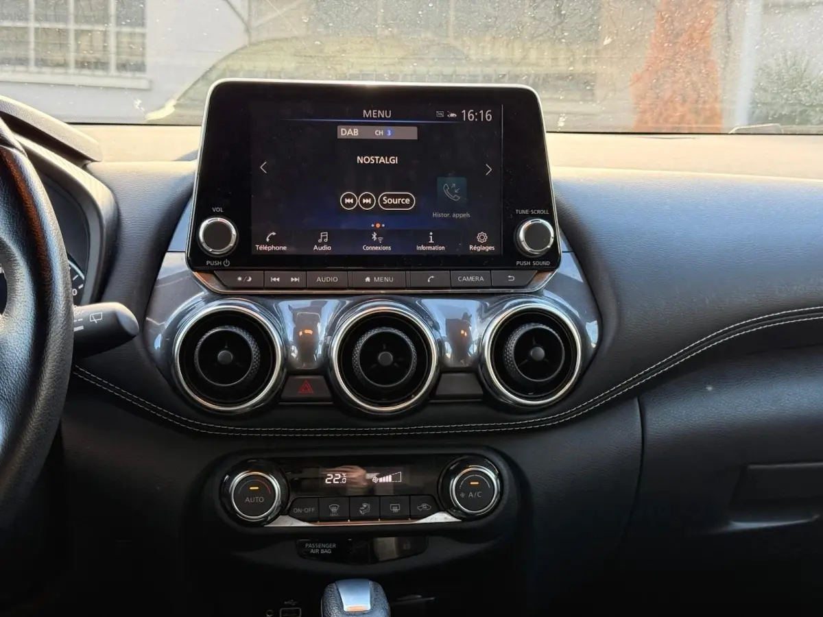 Tableau de bord du Nissan Juke 2023 avec écran tactile central, trois aérateurs ronds et commandes de climatisation.